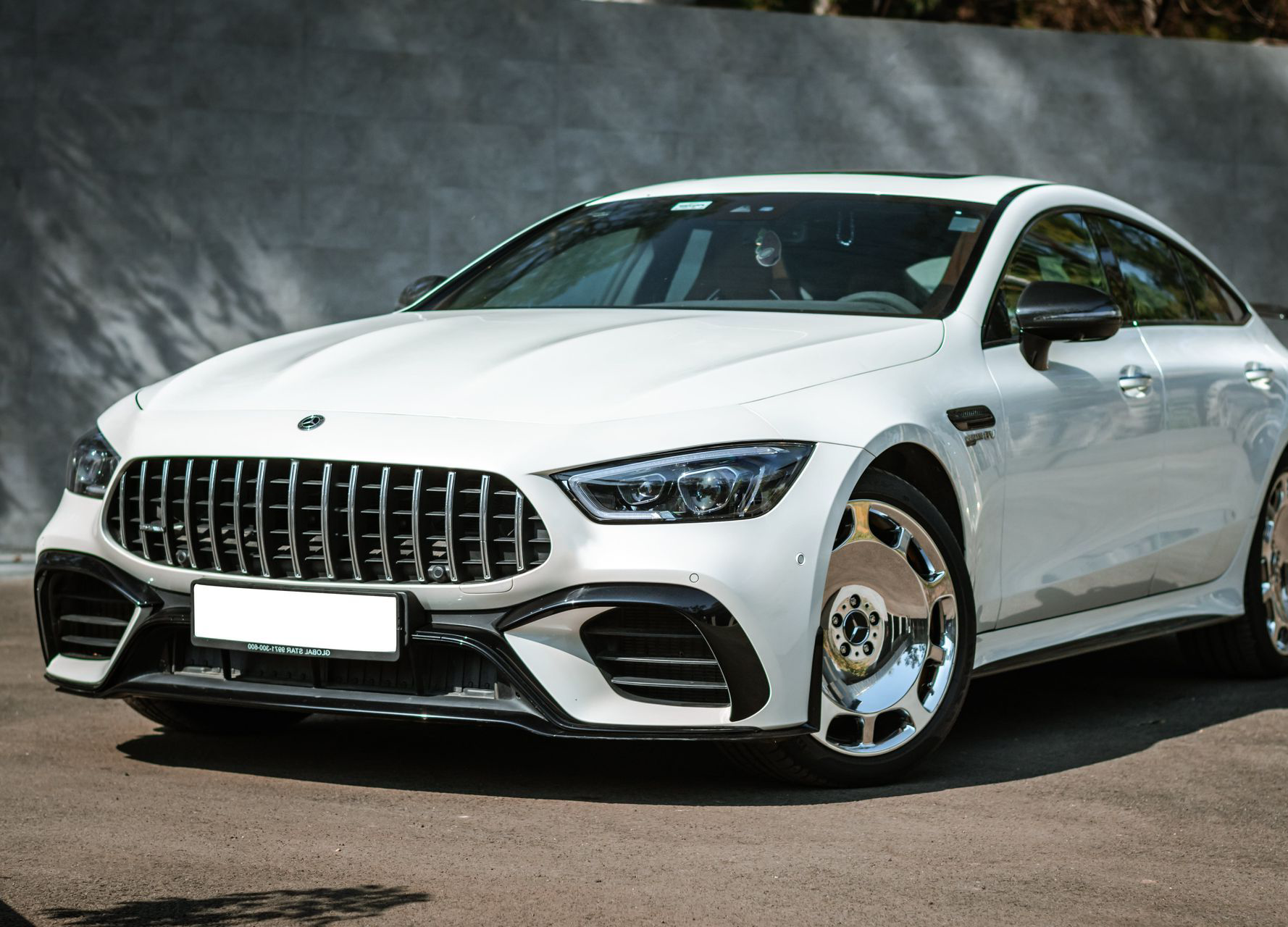 White Mercedes-AMG GT four-door coupe with chrome wheels, parked on asphalt.