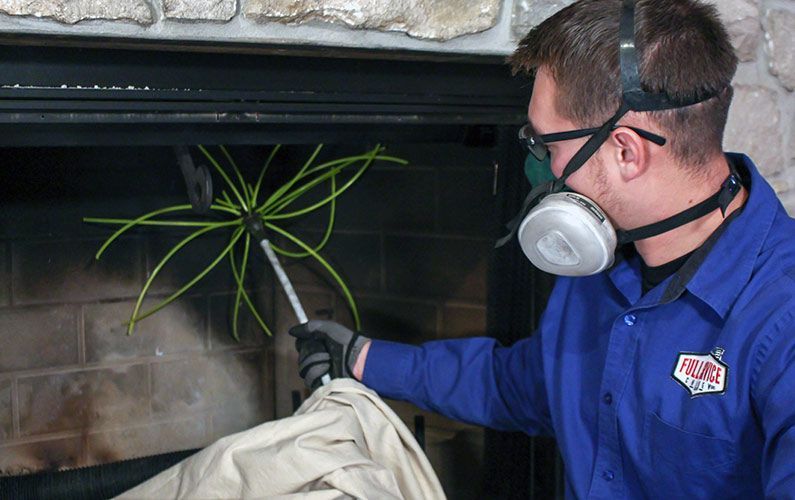A man wearing a mask and gloves is cleaning a fireplace.