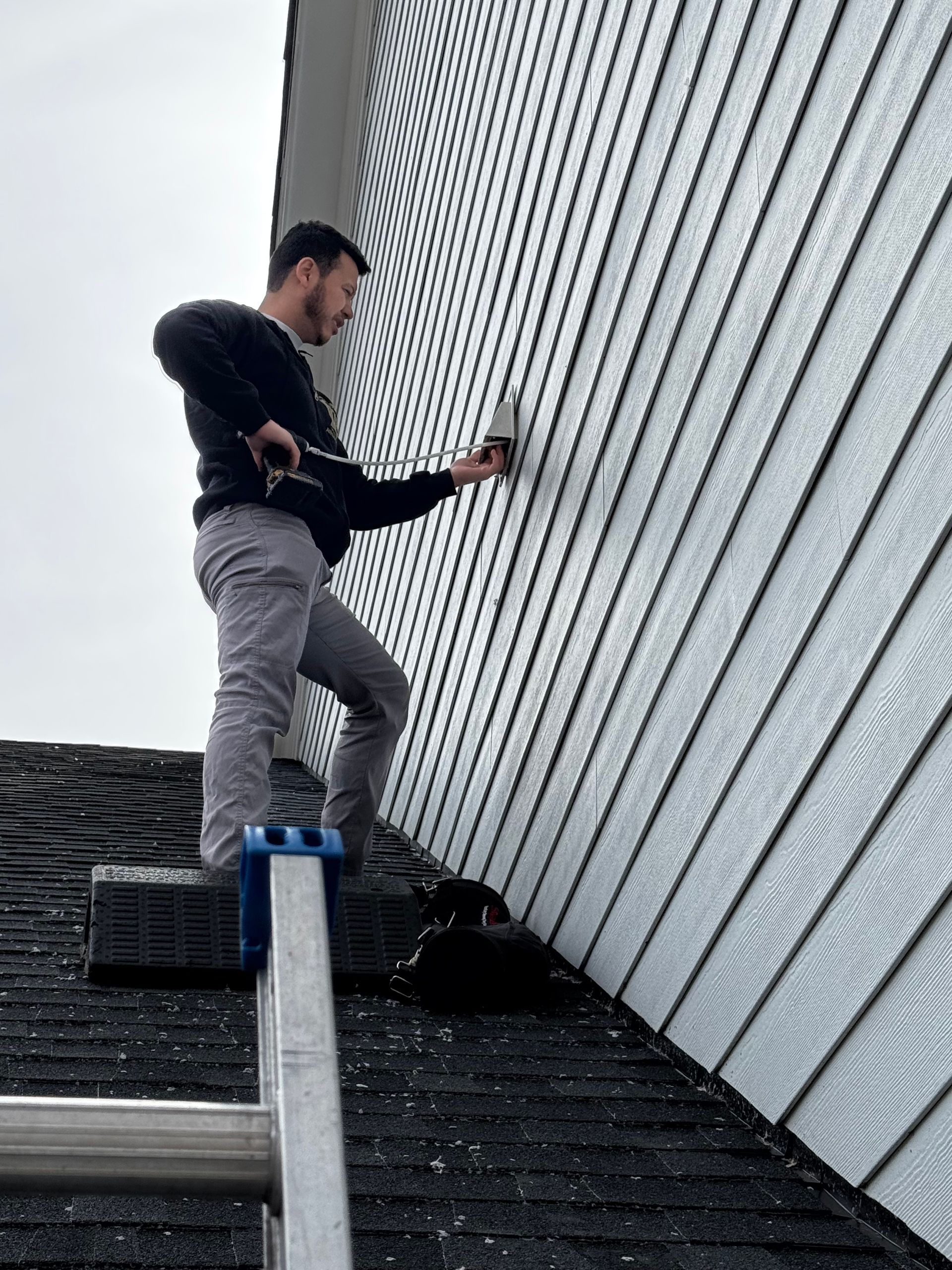 A man is standing on a ladder on the roof of a building.