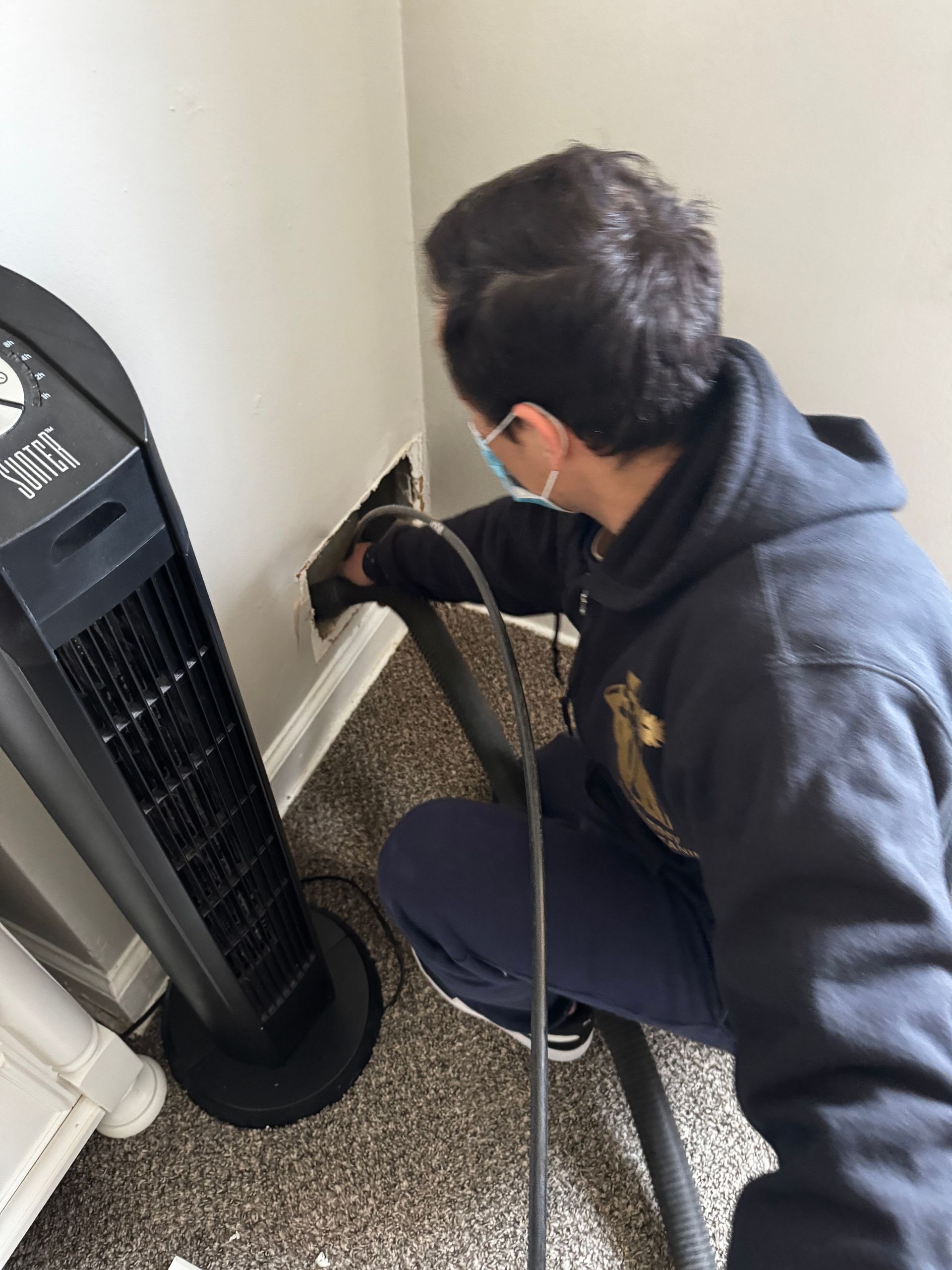 A man is using a vacuum cleaner to clean a fan in a room.