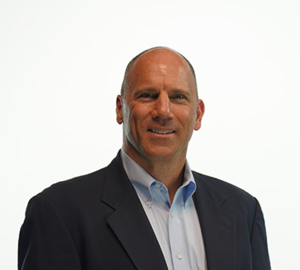 Man in a blue blazer and open-collared shirt, smiling, against a white background.