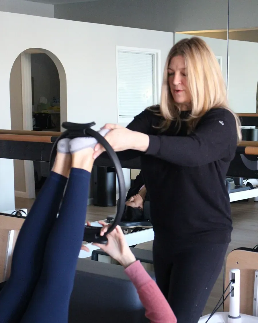 Physical therapist assisting a patient with leg exercises in a clinic, with mirrors and equipment nearby
