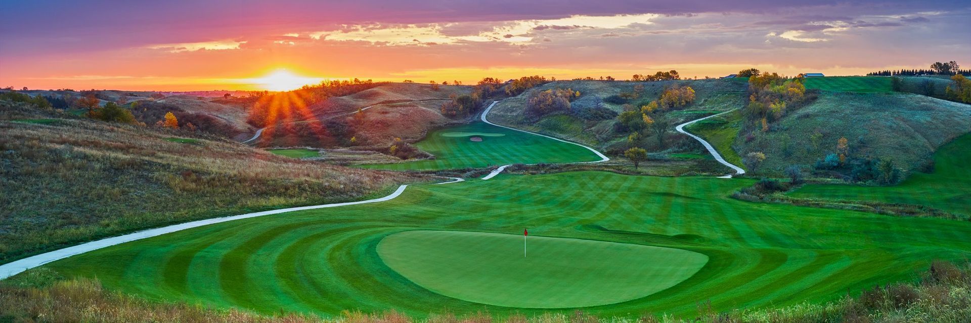 An aerial view of a golf course with a sunset in the background.
