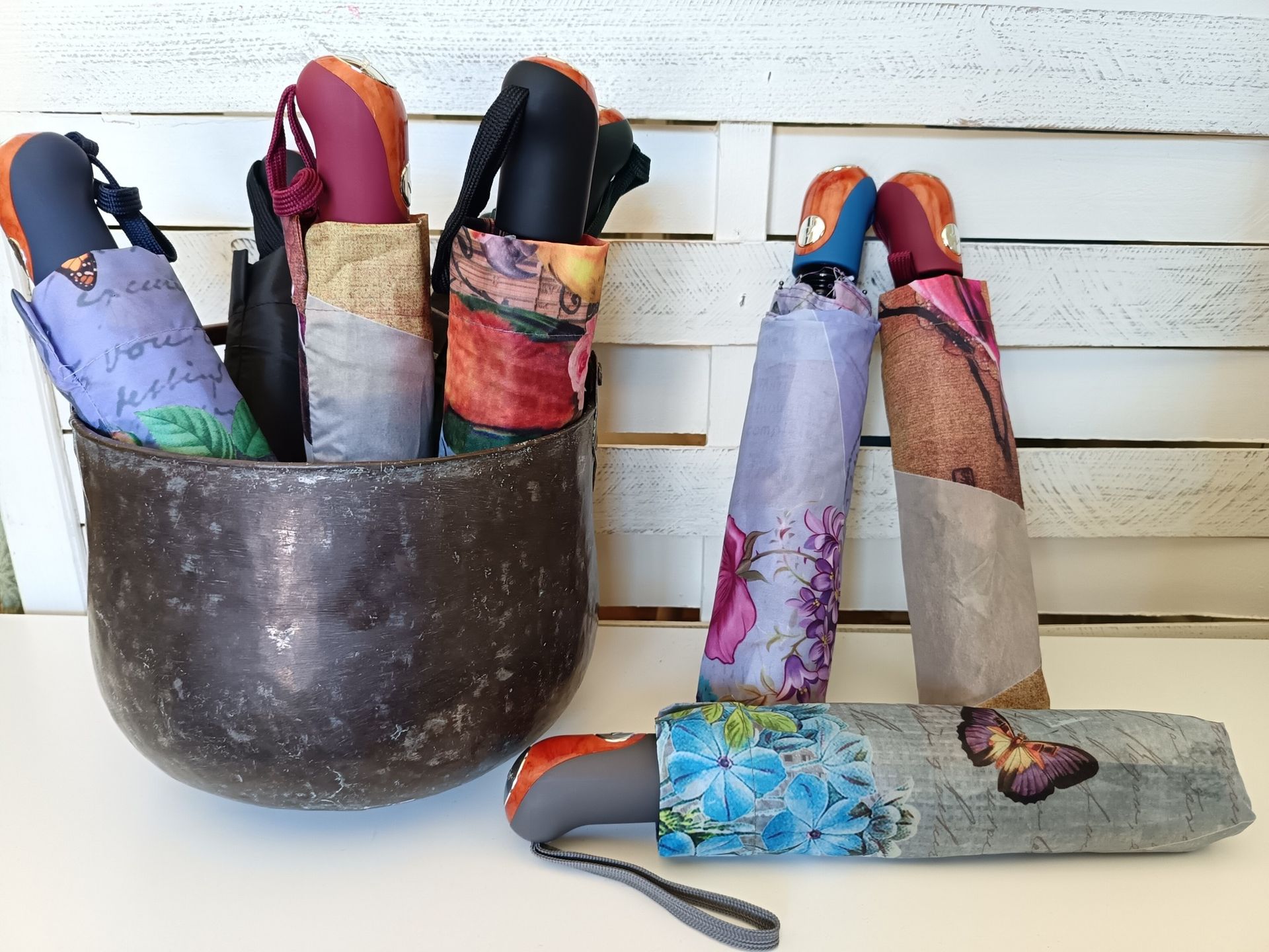 Diversi ombrelli colorati e decorati in un rustico contenitore di metallo e su una superficie bianca.