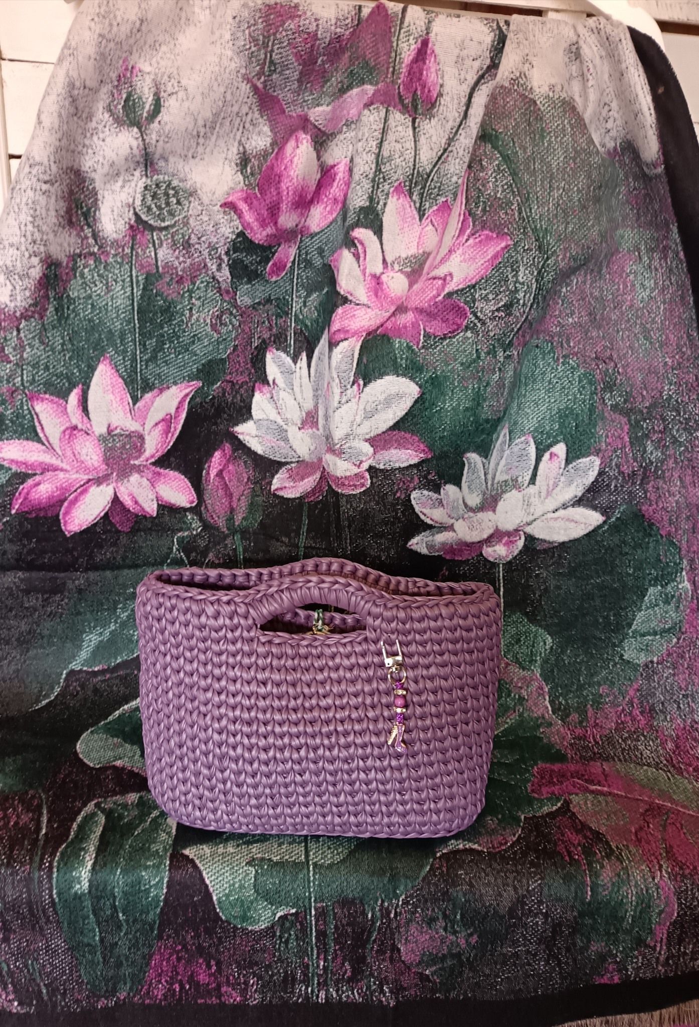 Cestino intrecciato viola con manici su uno sfondo floreale di fiori di loto rosa e bianchi.