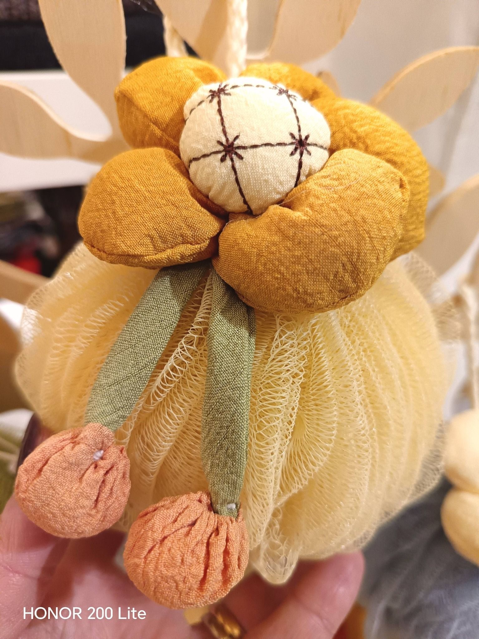 Luffa gialla con dettagli floreali gialli e arancioni e perline, tenuta in mano.