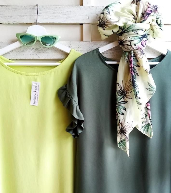 Due abiti appesi, uno verde chiaro e uno verde oliva, con occhiali da sole e una sciarpa floreale.