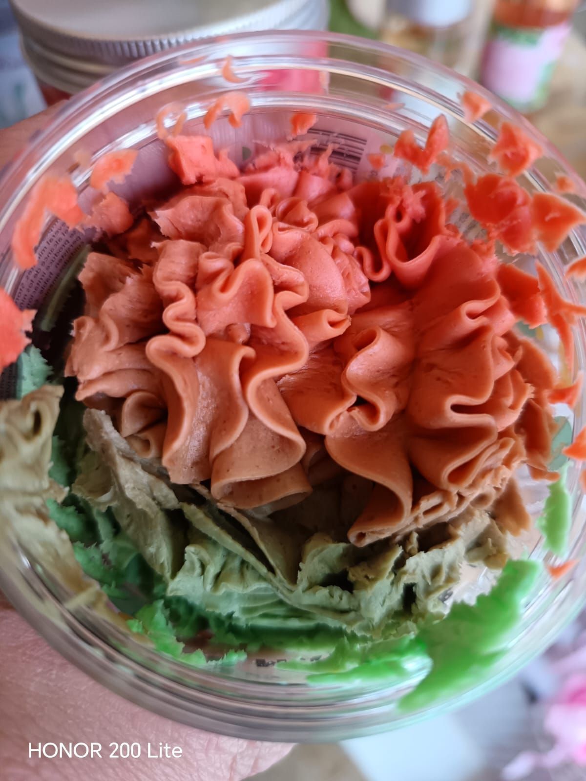 Primo piano del dessert in un contenitore trasparente, con strati di glassa verde, marrone e rossa in forme decorative.