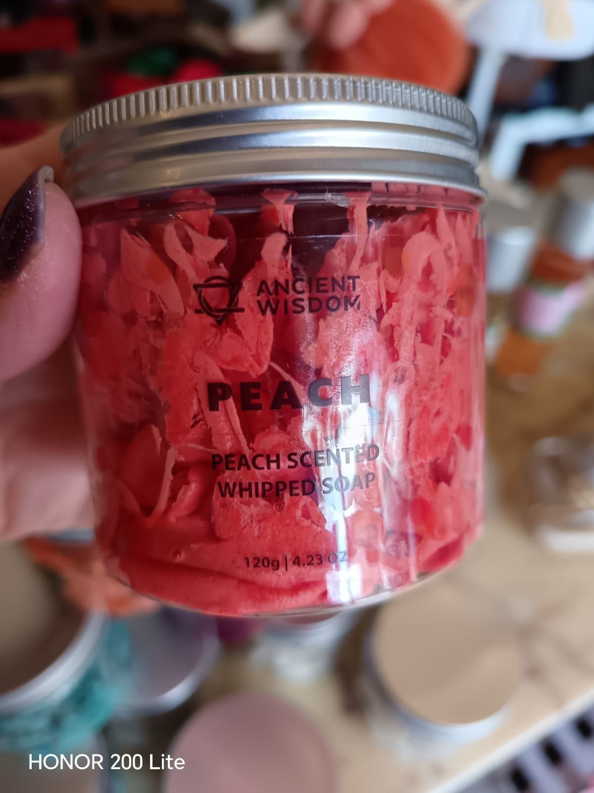 Barattolo di sapone montato al profumo di pesca rosa, tenuto in mano. Coperchio argentato, etichetta con la scritta 