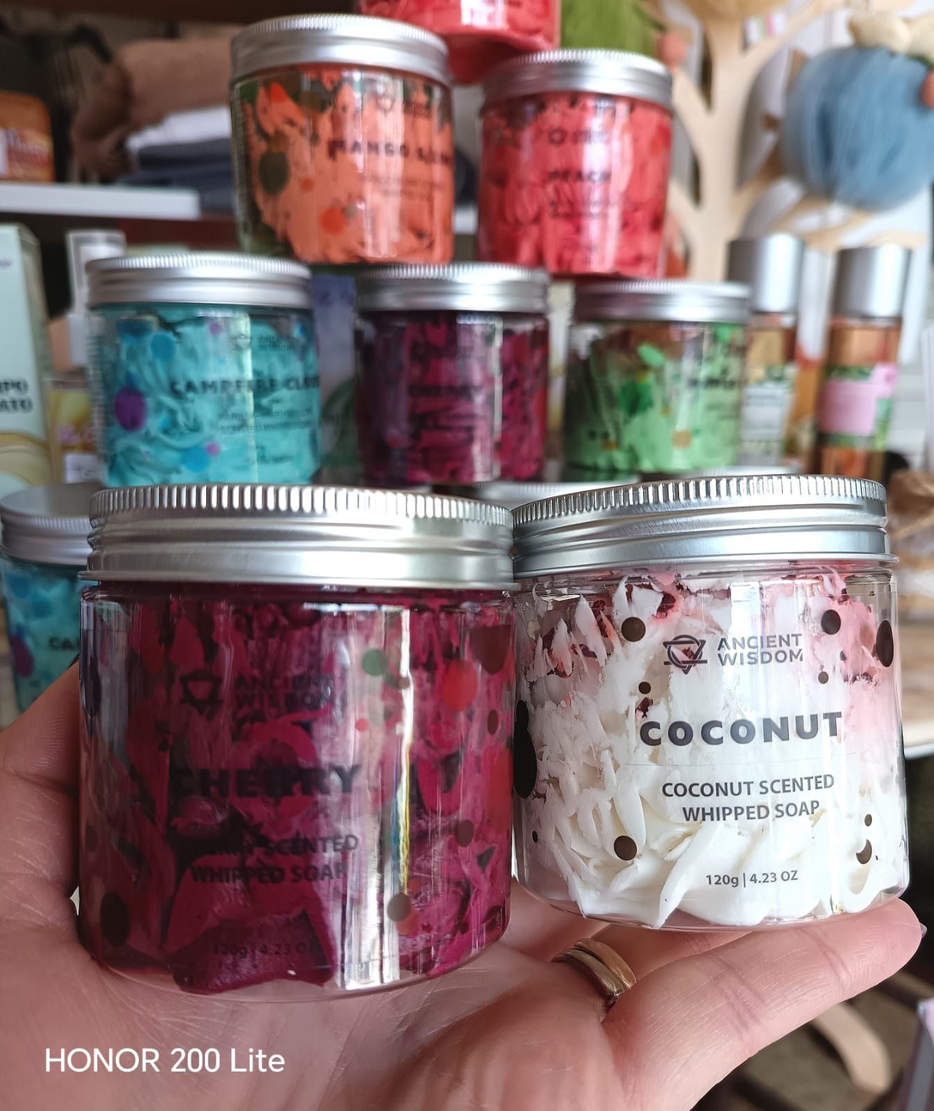 Mano che regge due barattoli di sapone colorato montato. Barattoli di vari colori sono esposti in un negozio.