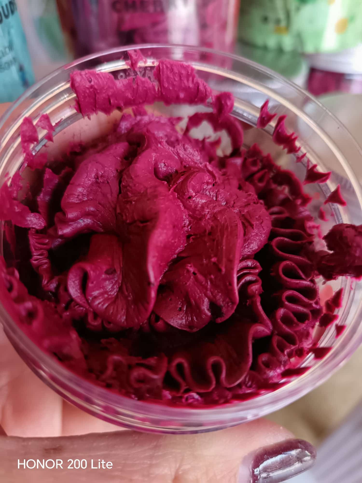 Un piccolo contenitore trasparente riempito con glassa rosa scuro a spirale.