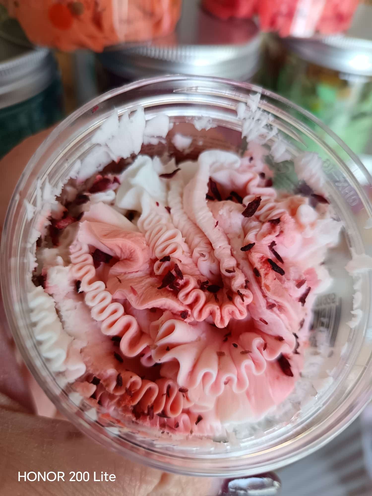 Dessert glassato rosa e bianco in un contenitore trasparente, decorato con granelli di zucchero scuri.