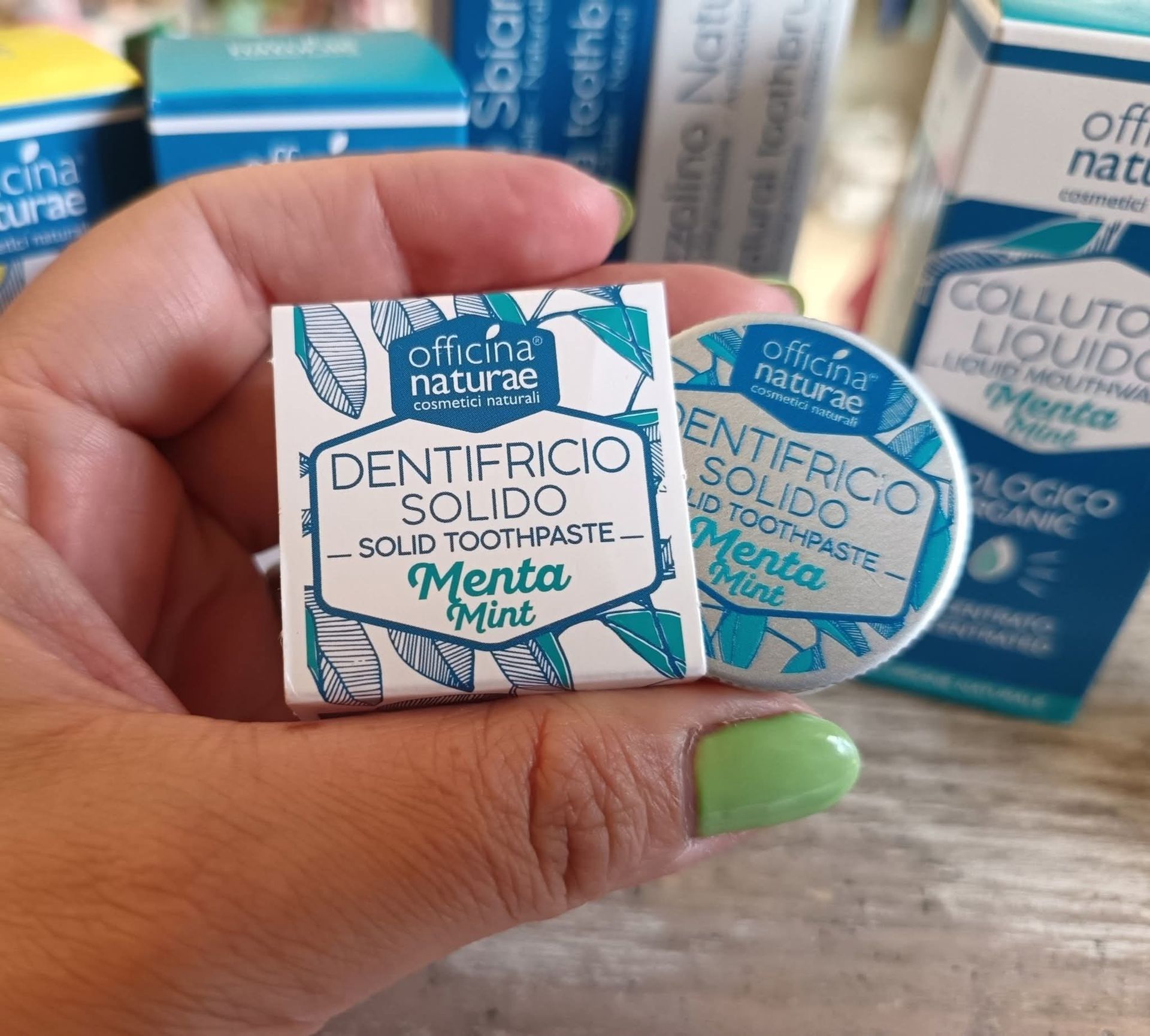 Mano che regge due piccoli contenitori di dentifricio solido al gusto di menta. Sono bianchi con dettagli blu e la scritta