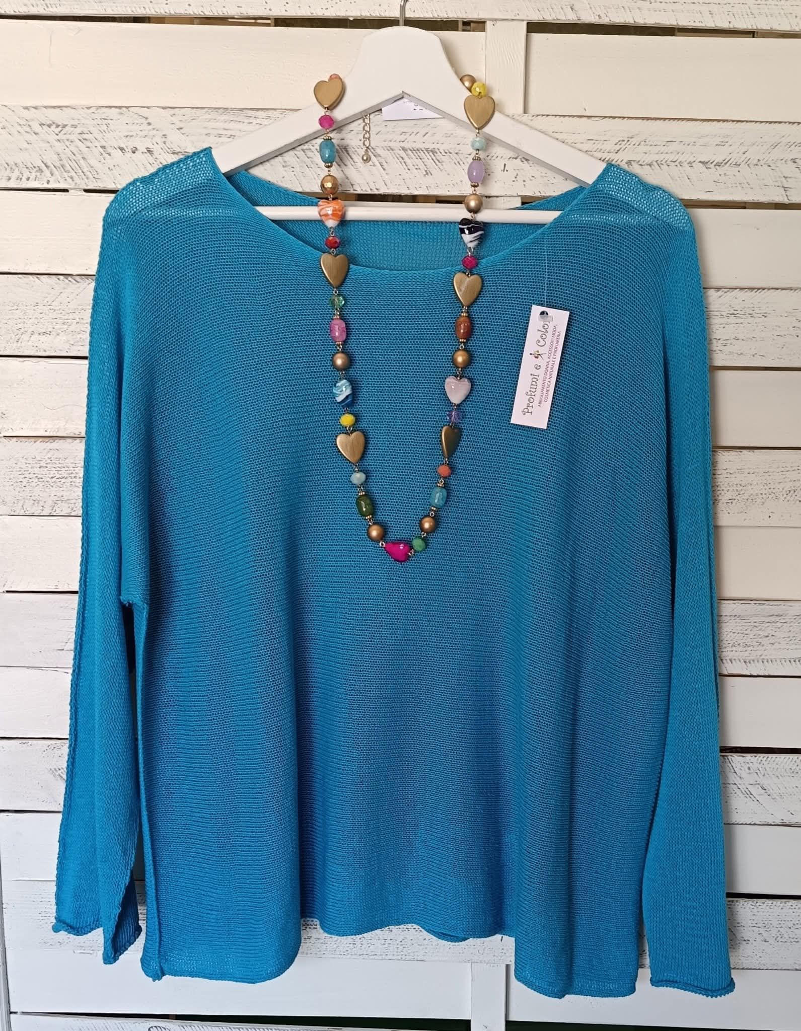 Maglia a maniche lunghe color verde acqua appesa a un attaccapanni bianco con una collana di perline colorate.