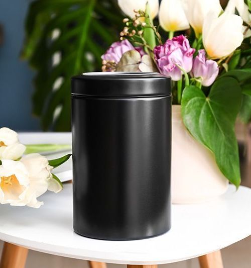 A black can is sitting on a table next to a vase of flowers.