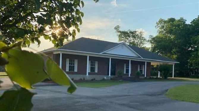 A large brick house with a porch and a tree in front of it.