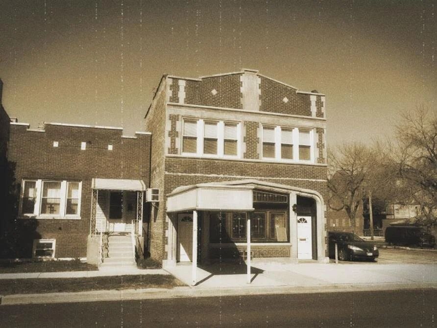 A black and white photo of a building with a car parked in front of it