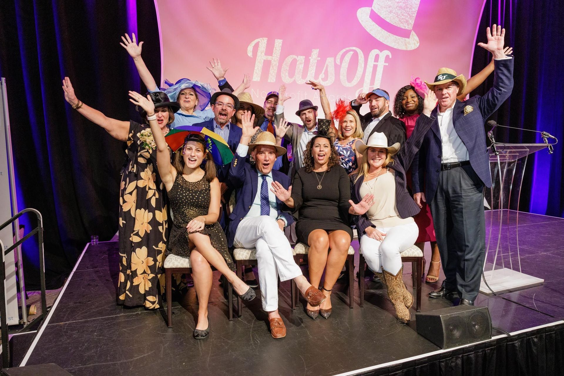 Group of people with hats sit in chairs with hands raised