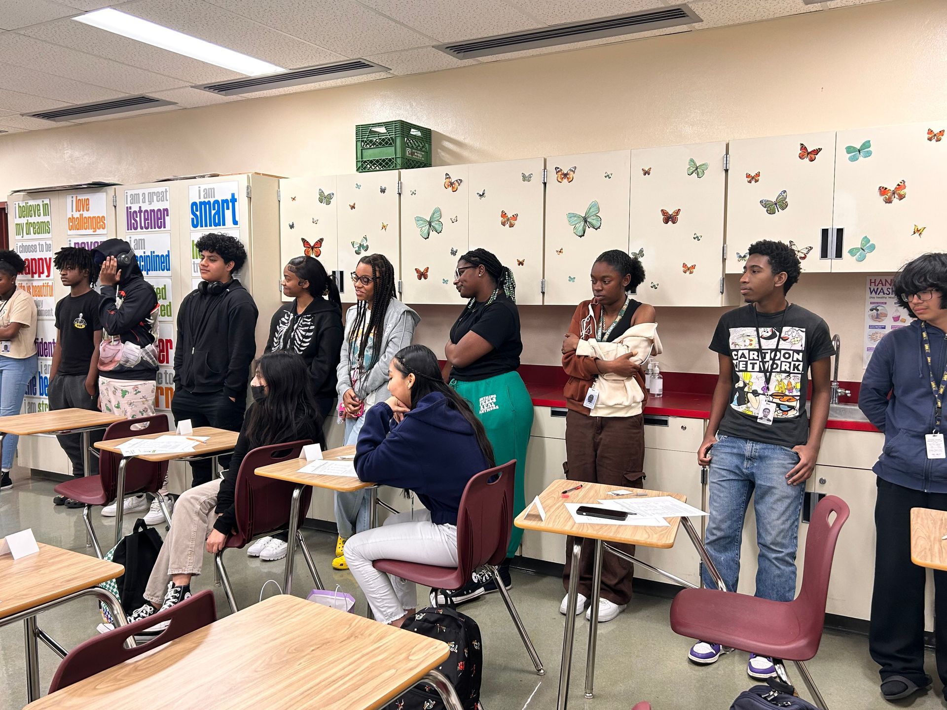 A group of students standing at back of classroom