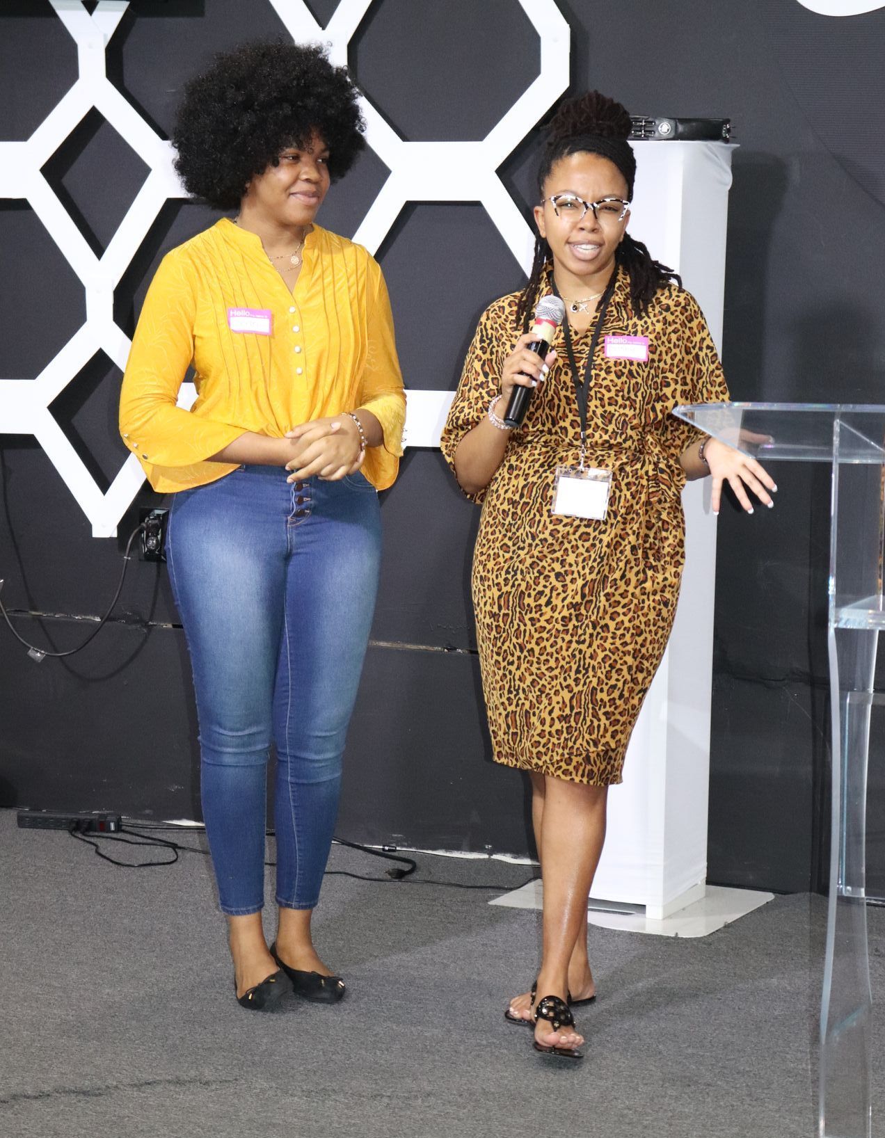 Two women standing one is holding a microphone