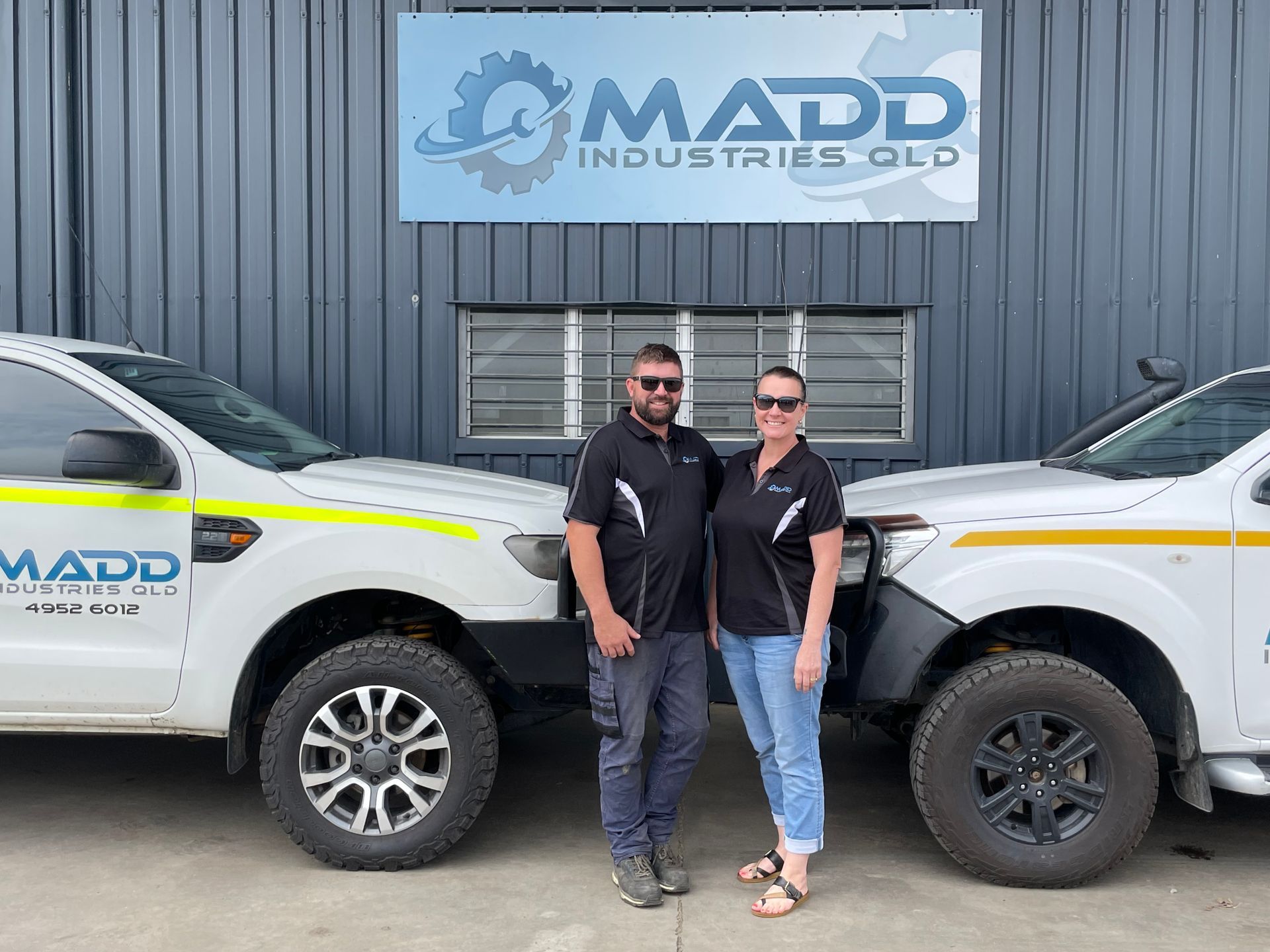 A man and a woman are standing next to two trucks in front of a building.