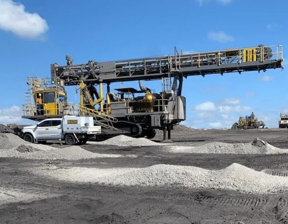 A white truck is parked next to a large machine in a dirt field.