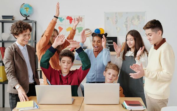 A group of children are standing around a table with laptops in a classroom.