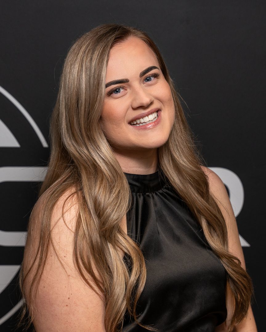 A woman with long hair is wearing a black top and smiling.