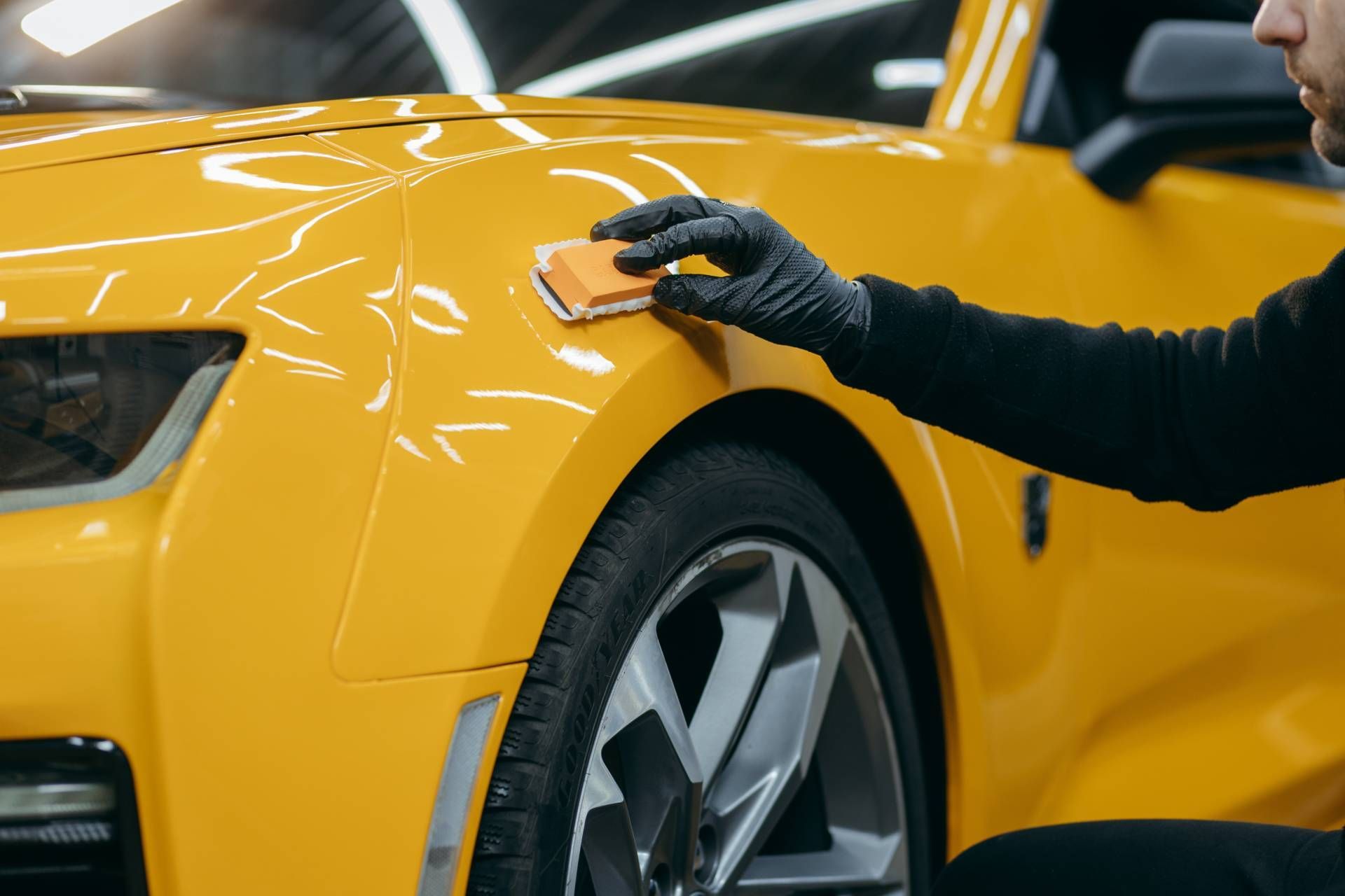 A person in gloves applies a ceramic coating to a yellow car's fender.