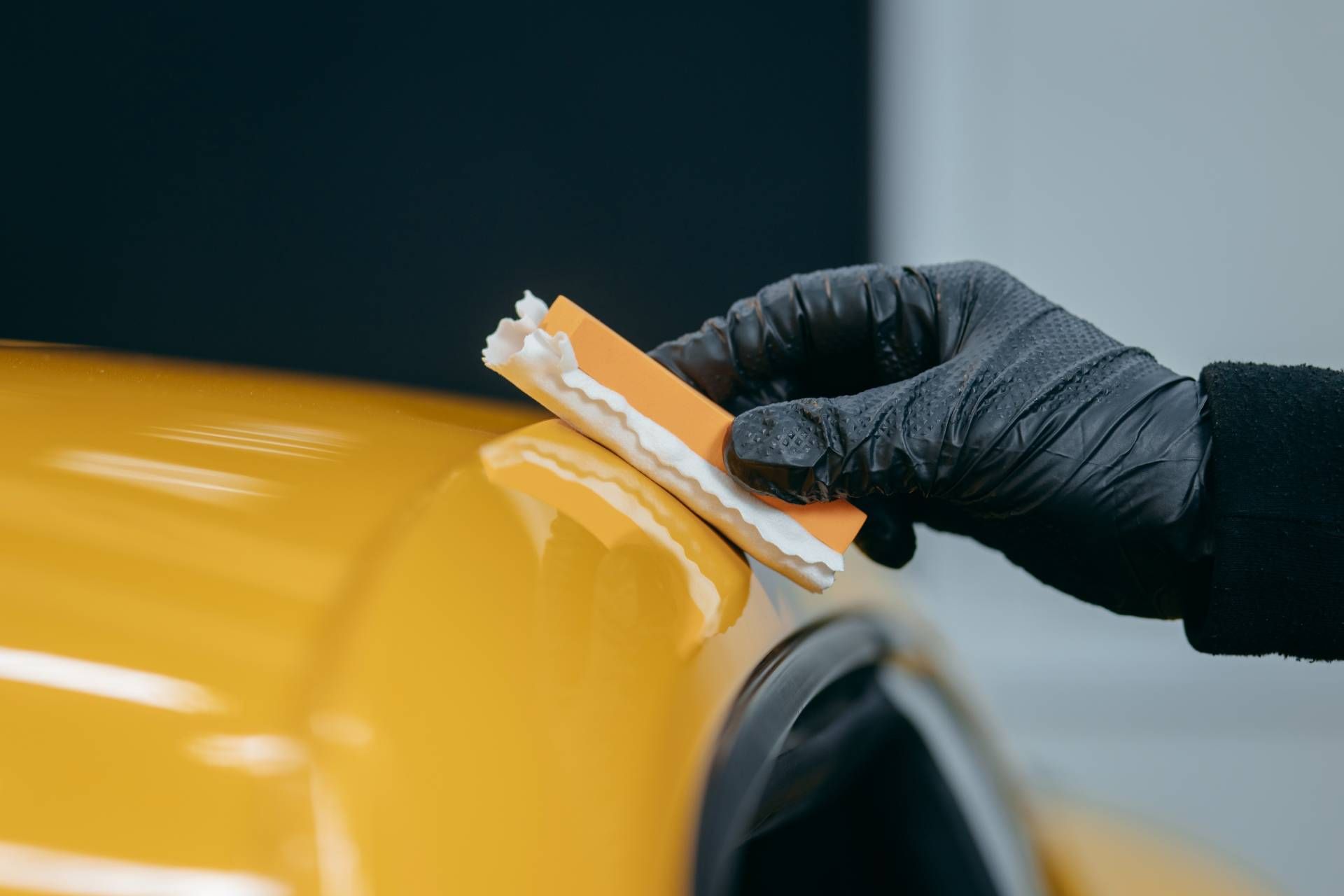 Gloved hand applying ceramic coating to yellow car panel with an applicator.
