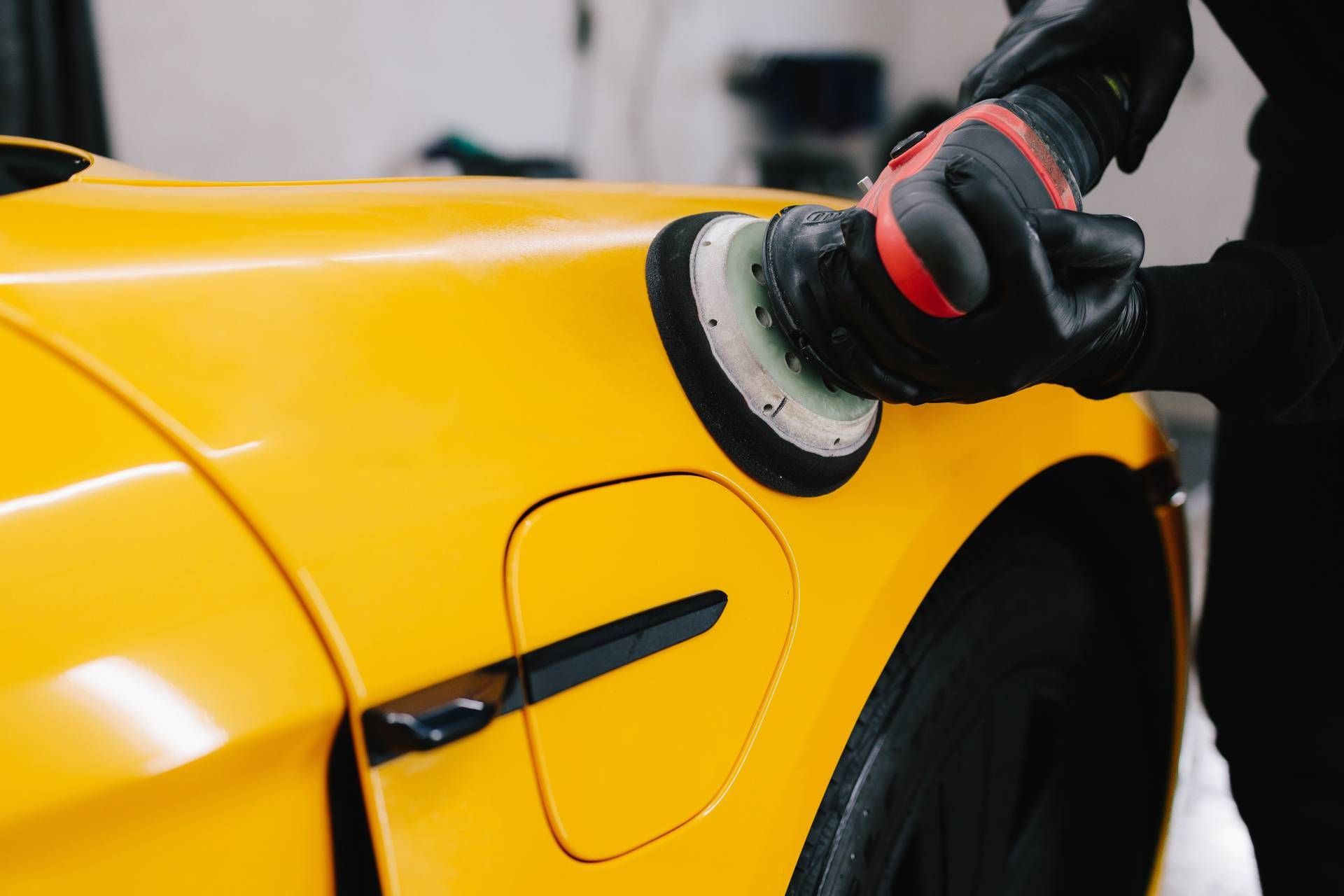 A person polishing a bright yellow car with a power buffer.