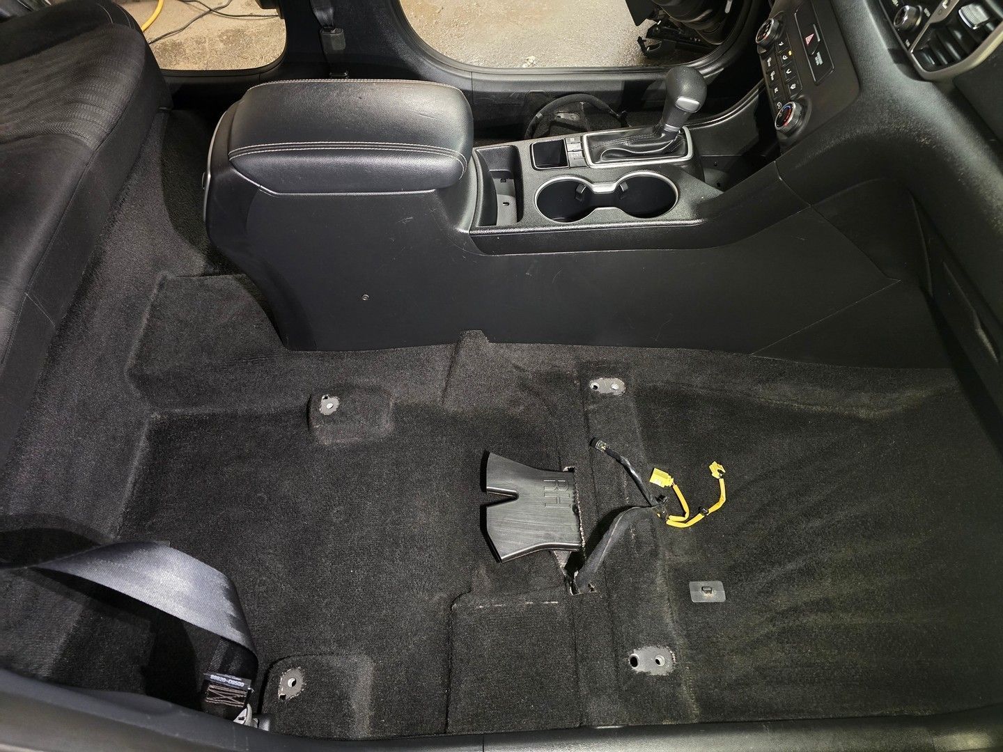 Black car interior with the carpet removed, revealing the floor. Center console and seats are present.