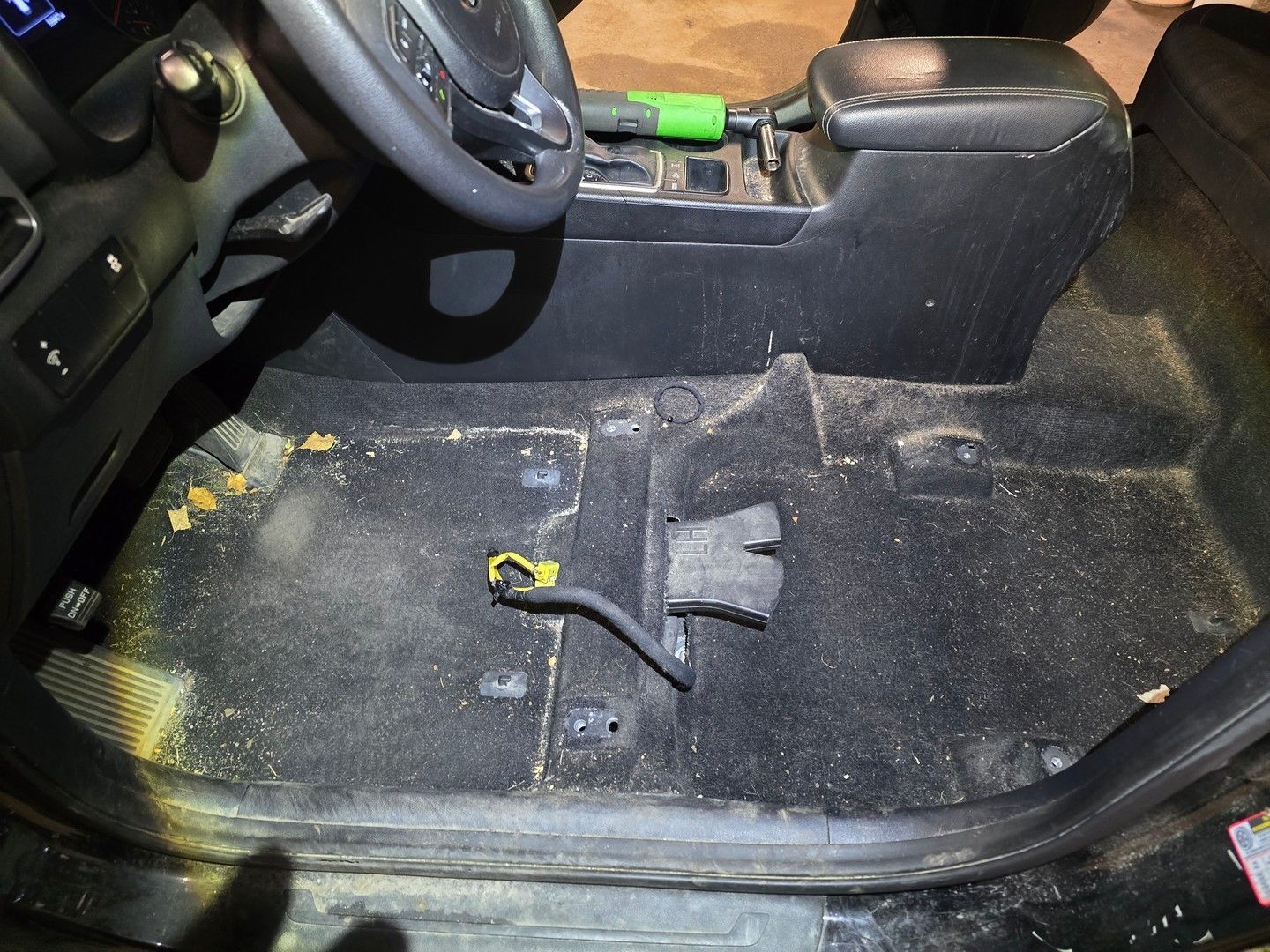 Dirty car interior with black carpet, steering wheel, and center console. Debris and dust are visible.