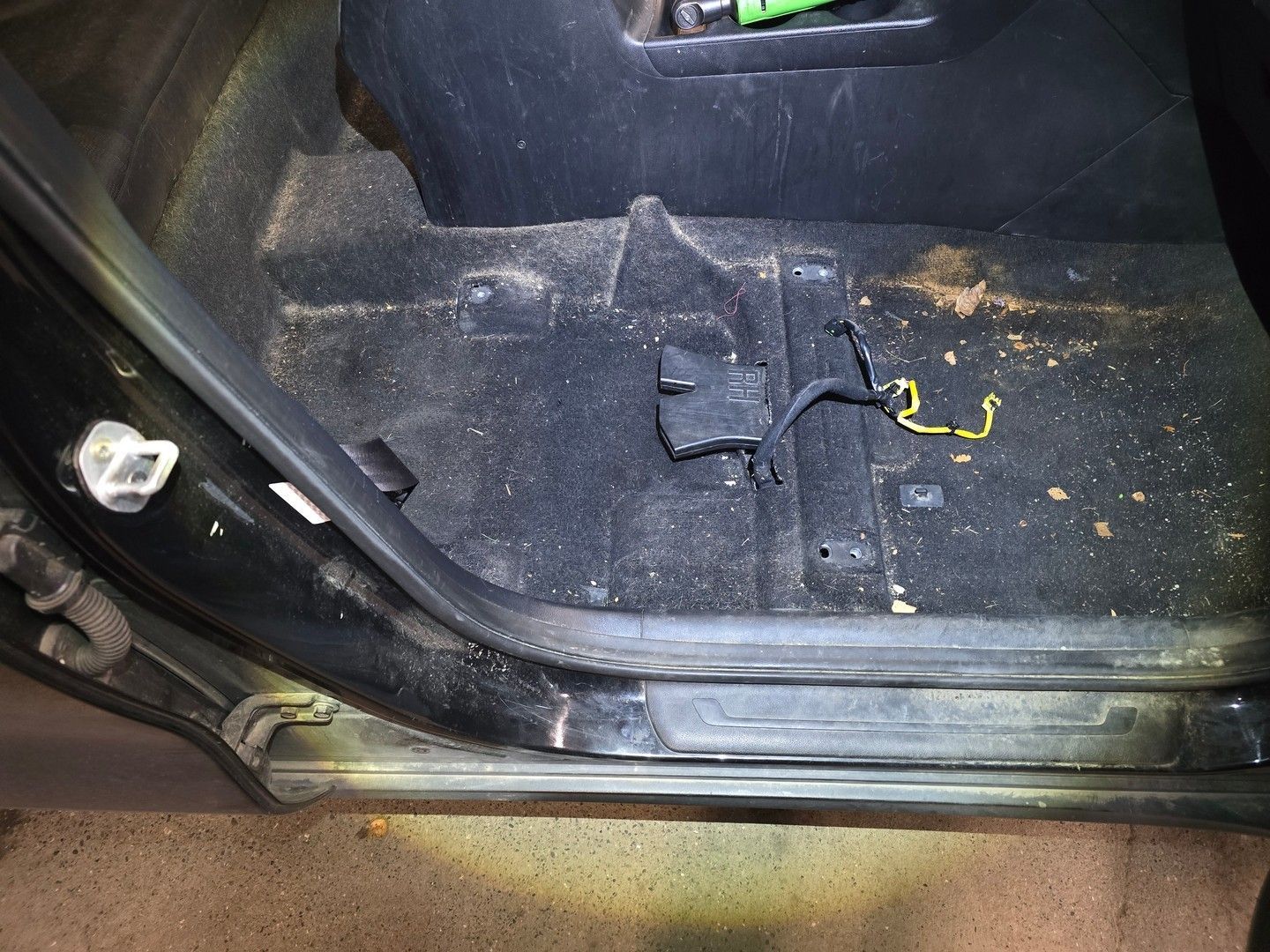Black car interior with exposed wires and debris on the carpet.