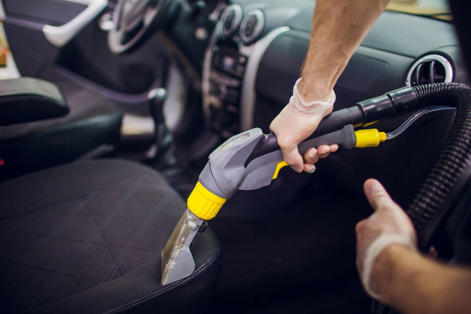 Person vacuuming a car seat with a handheld vacuum cleaner.