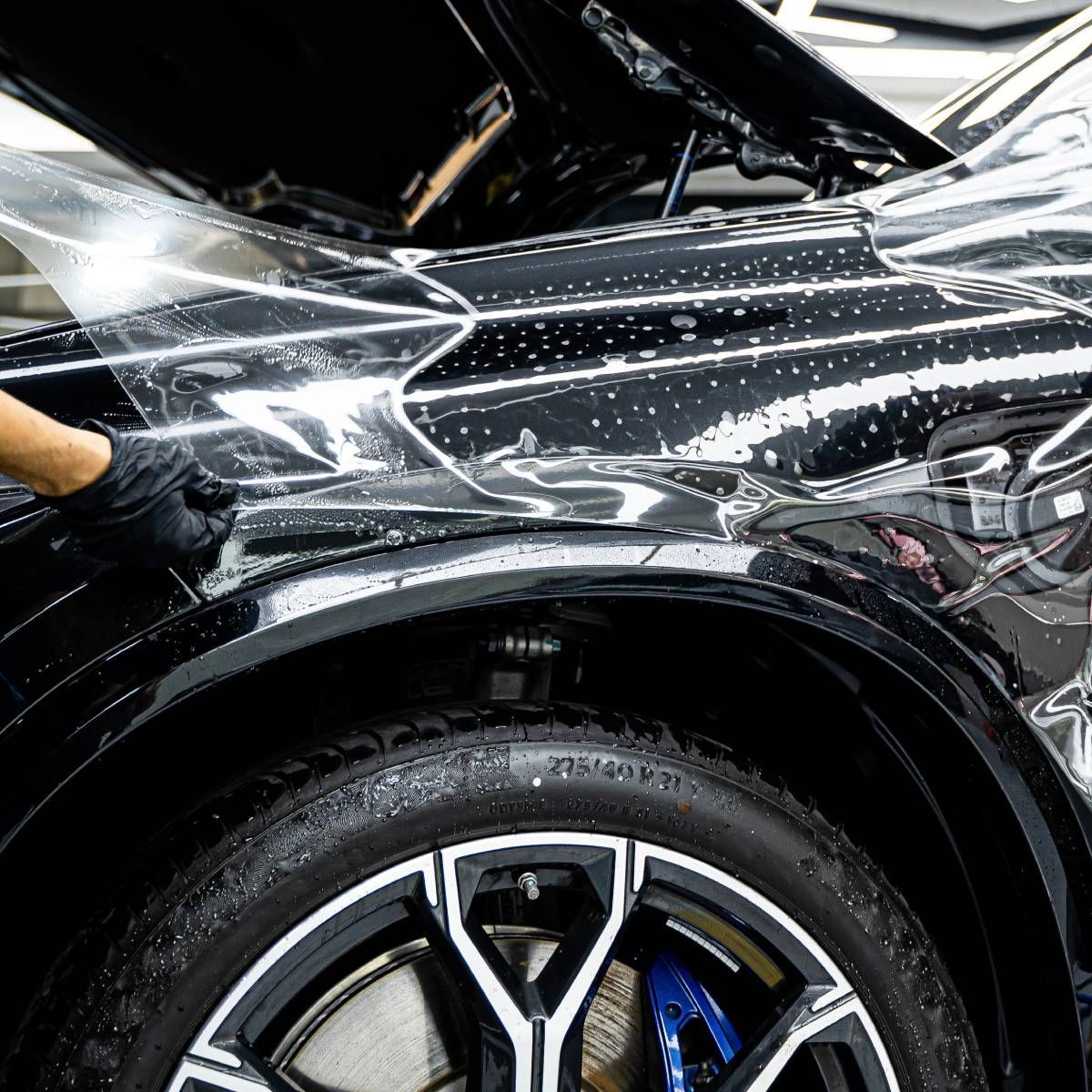 Black car being detailed; installer applying clear protective film.