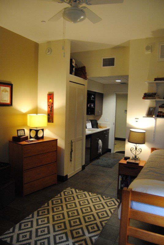 View of a dorm room with dresser, desk and bed.