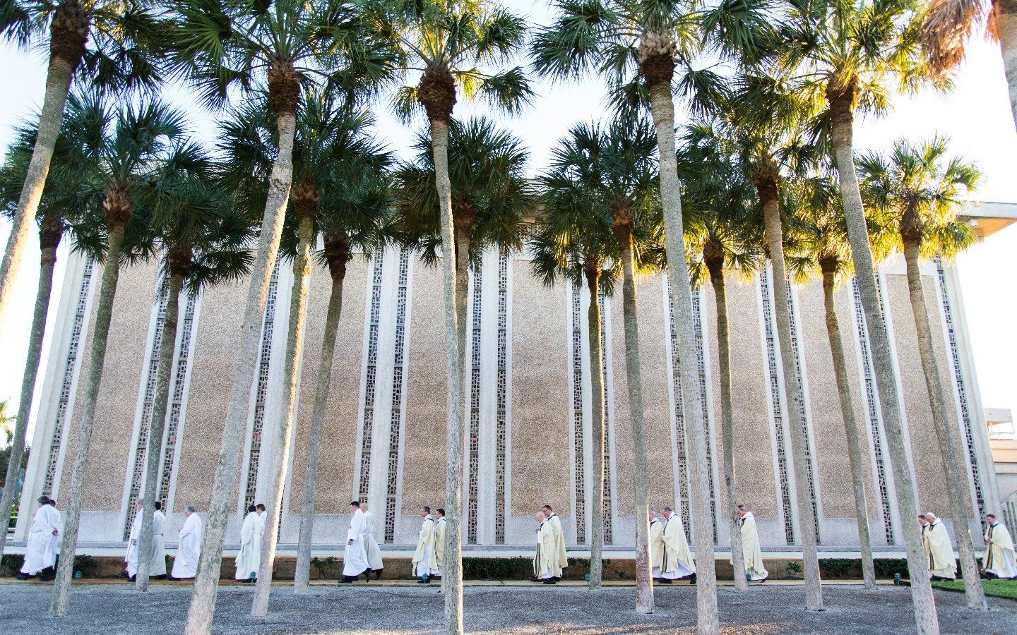 Priests walking in front of chapel and palm trees