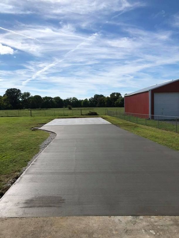 A concrete driveway with a red barn in the background.