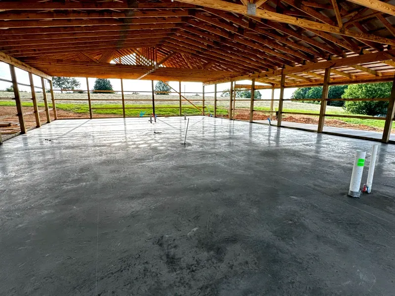 A large concrete floor under a wooden roof in a building under construction.