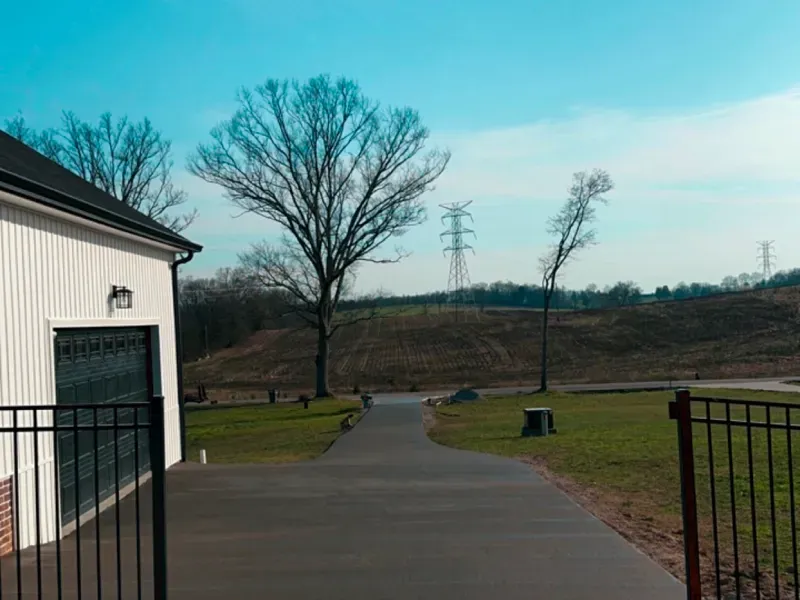 A road leading to a house with a fence and trees on the side of it.