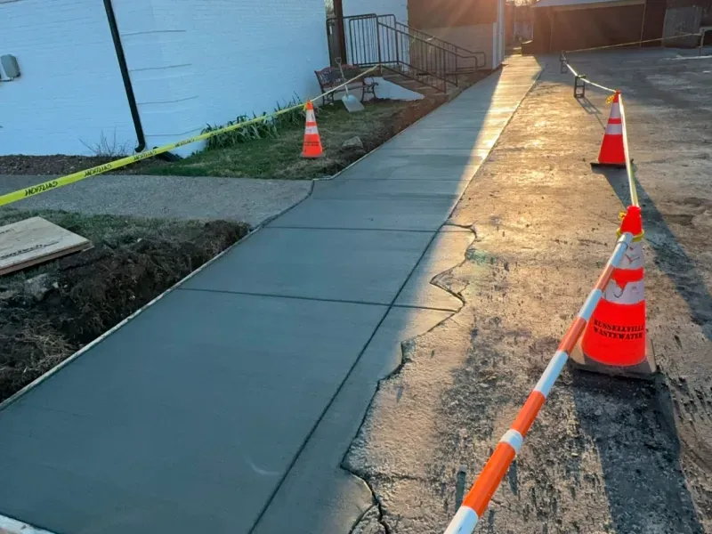 A sidewalk is being built with orange and white traffic cones.