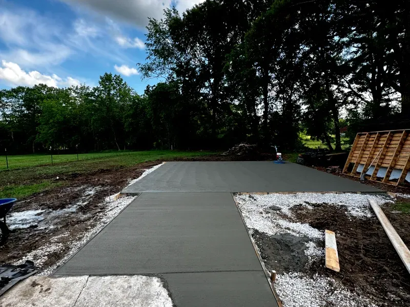 A concrete driveway is being built in a field with trees in the background.