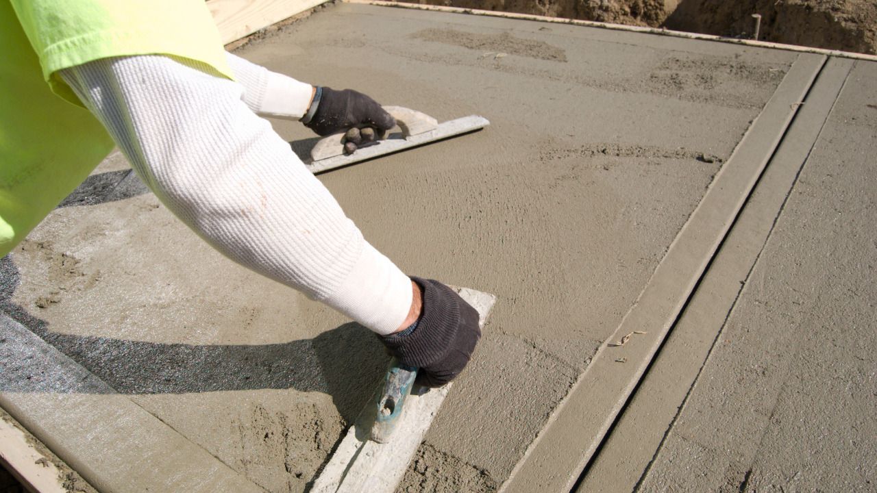 A man wearing a hat is laying bricks on a sidewalk.