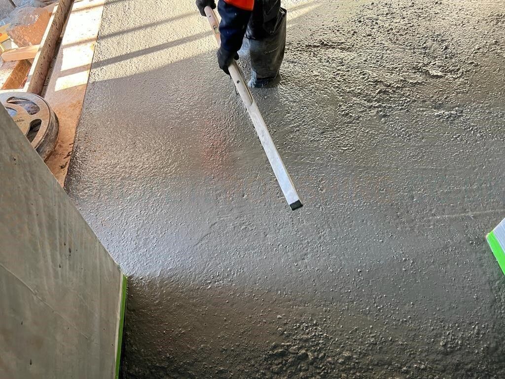 A man is using a shovel to spread gravel on a patio.