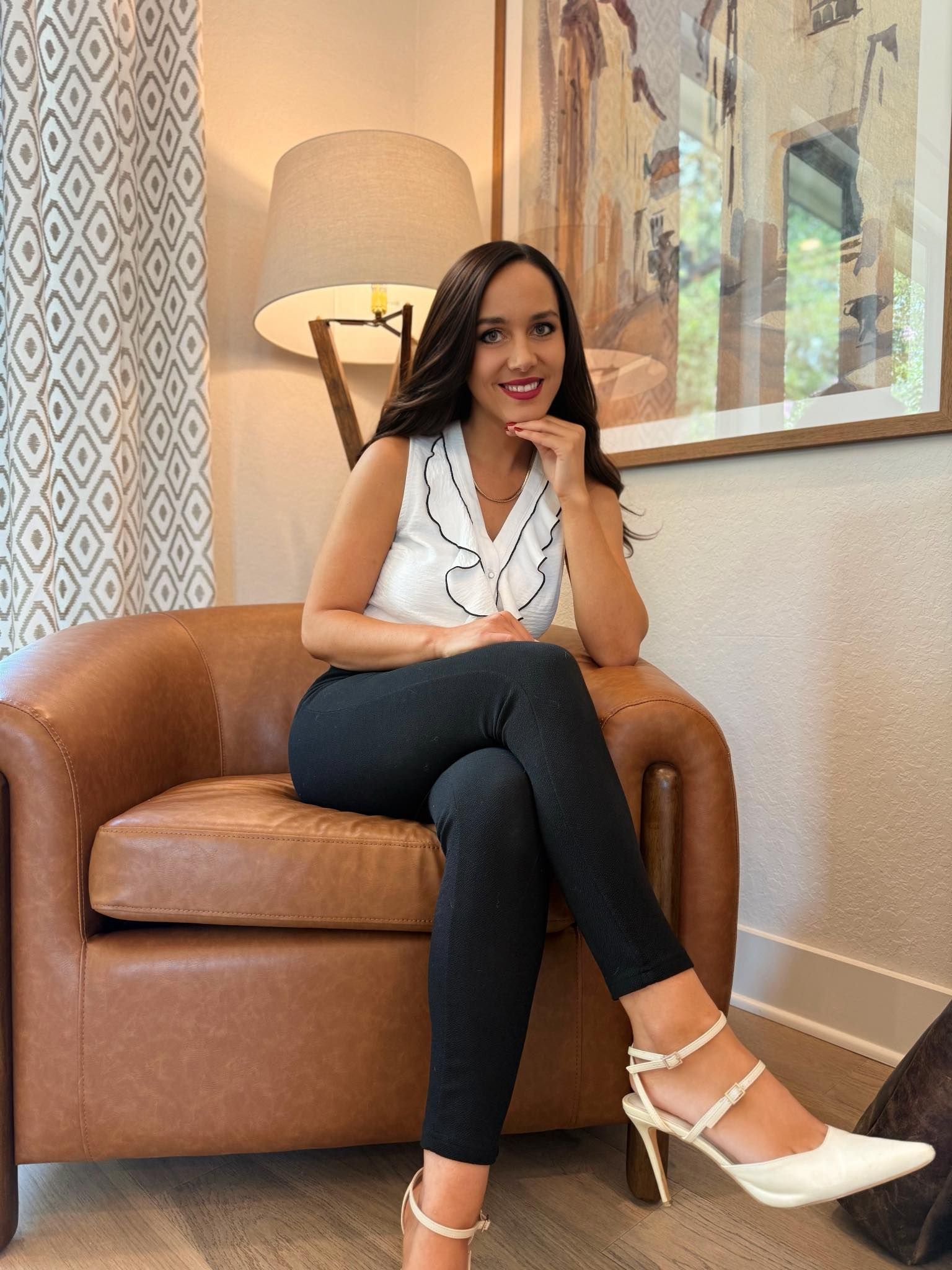 A woman is sitting at a desk with a laptop and a vase of flowers.