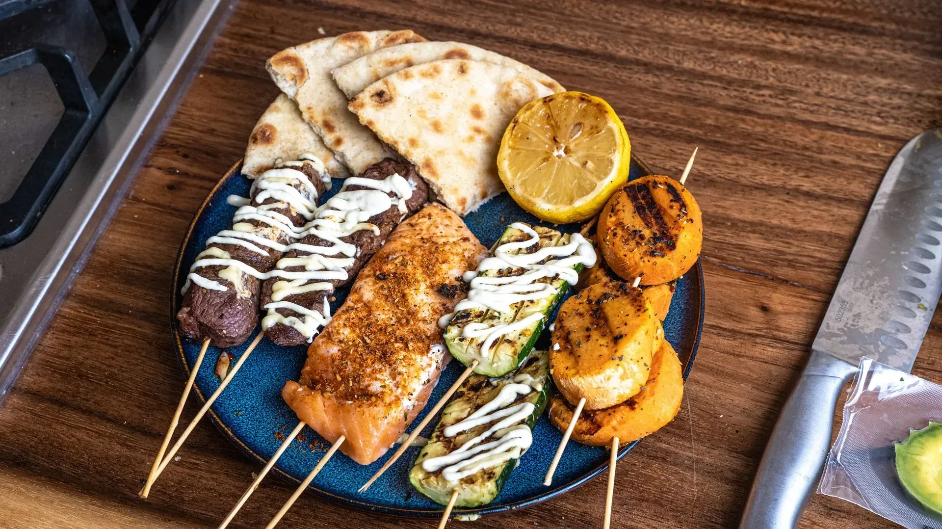 A plate with meat and vegetables on sticks next to some bread