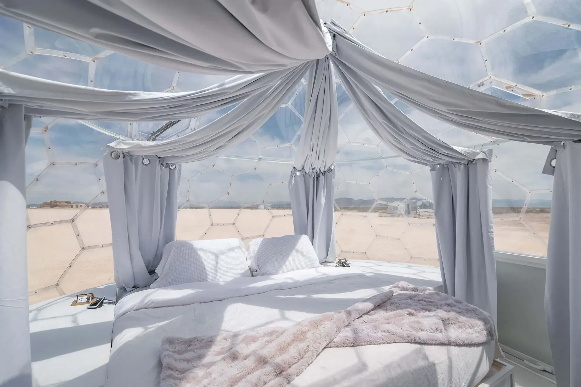 A bed in a dome with white curtains and a view of the desert.