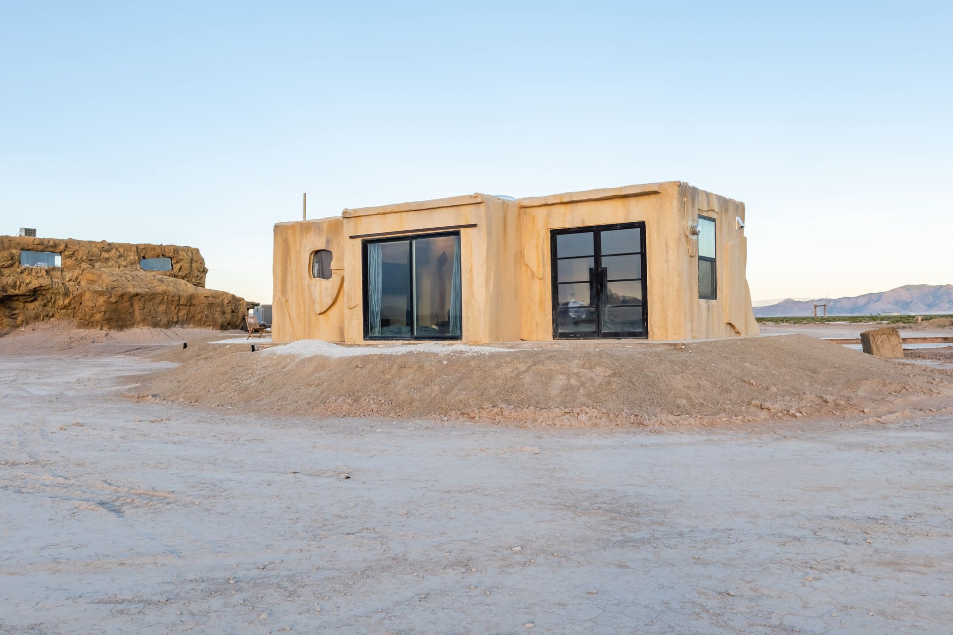 A small house is sitting on top of a dirt hill in the desert.
