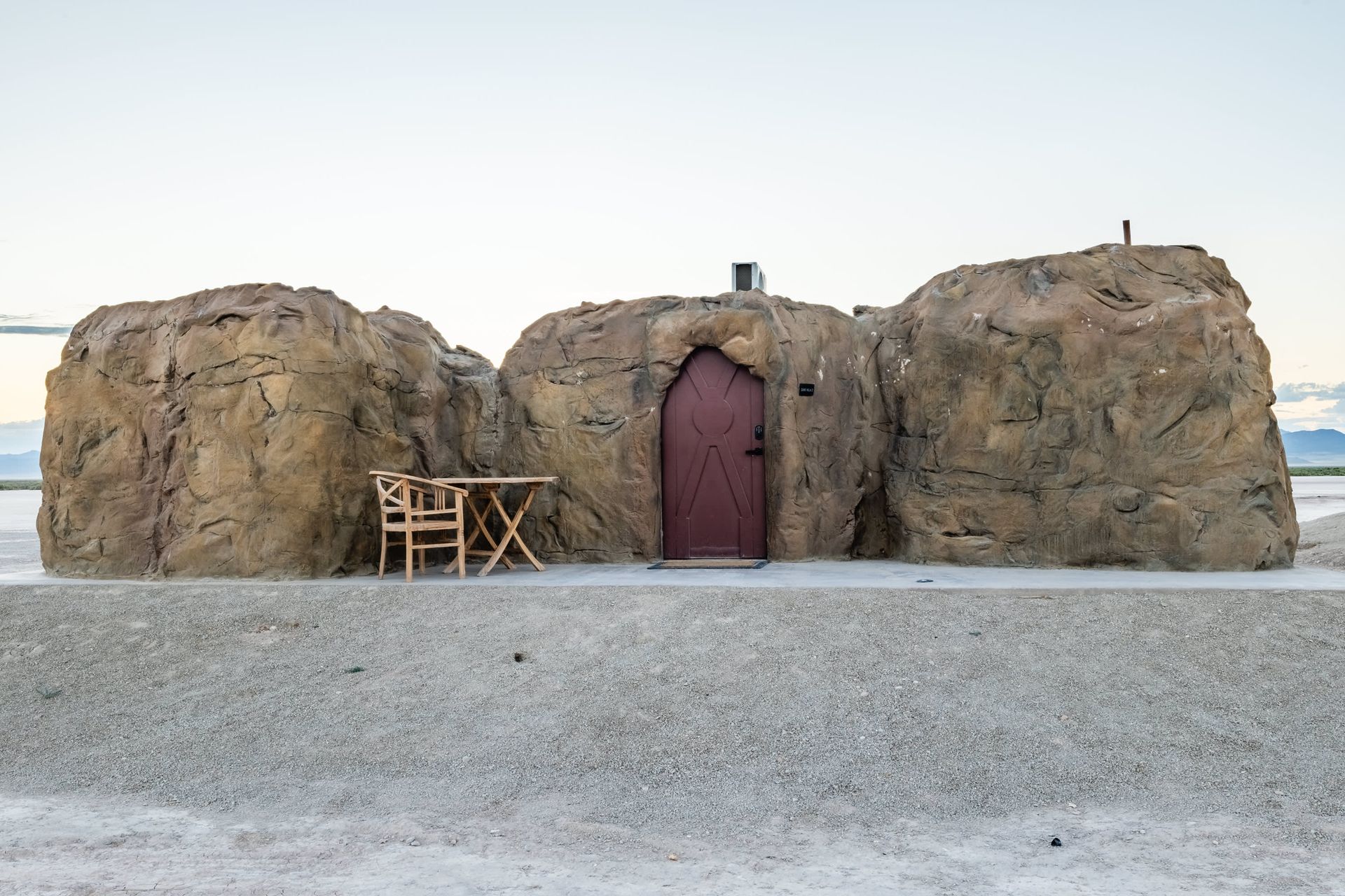 A house made out of rocks with a red door and a table and chairs in front of it.